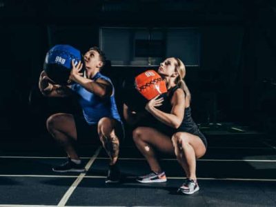 Young athletic man and woman squatting with weighted balls at gym